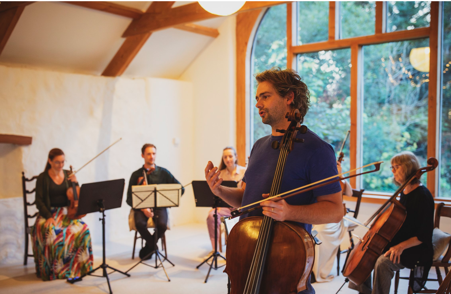 String quintet playing in a room lit by a large window overlooking a garden.