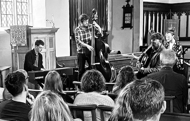 Jazz quartet playing their instruments; guitar, bass drums, keyboards.