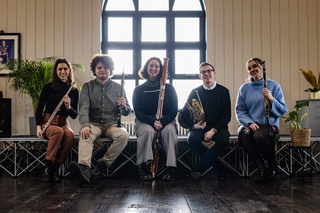 The Bute Wind Quintet holding their instruments in front of a window of the Norwegian Church Arts Centre, Cardiff Bay.